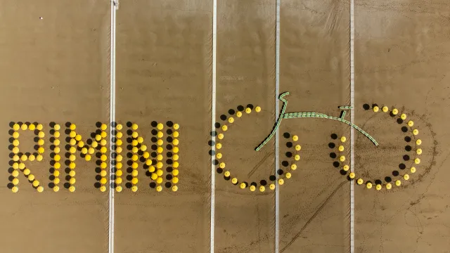 scritta rimini in giallo sulla spiaggia con gli ombrelloni